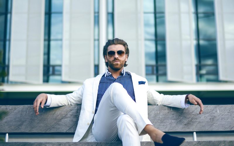 pexels-photo-2709563-2709563 Fashionable man in white suit sitting confidently on a bench outdoors, embodying elegance and modern lifestyle.